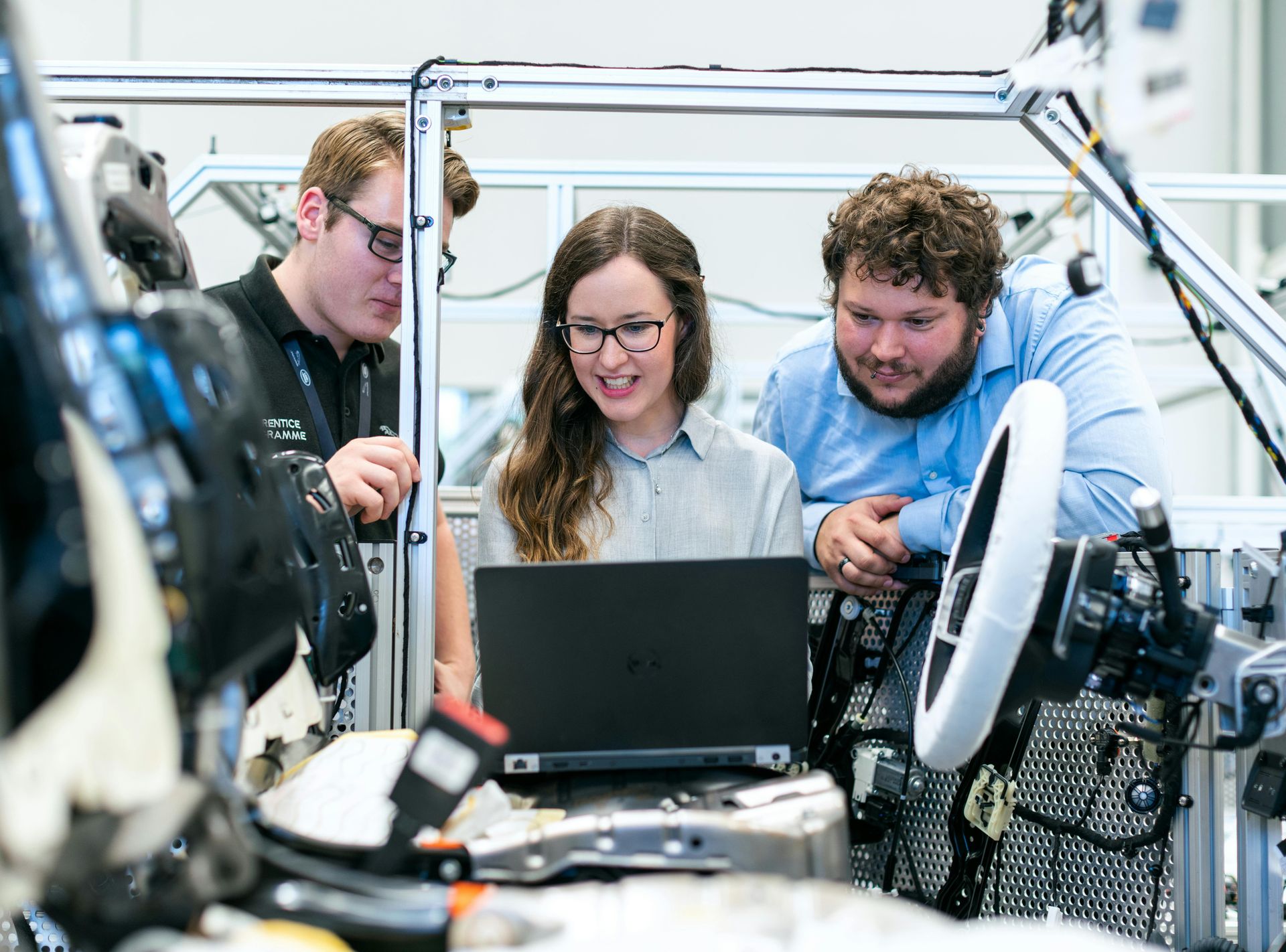 Three people stand around a laptop resting on an electric vehicle